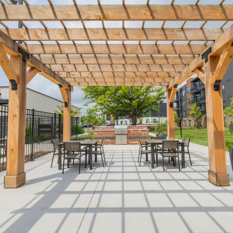 Outdoor covered cabana lounge shading a patio with dining tables and a brick barbecue station.