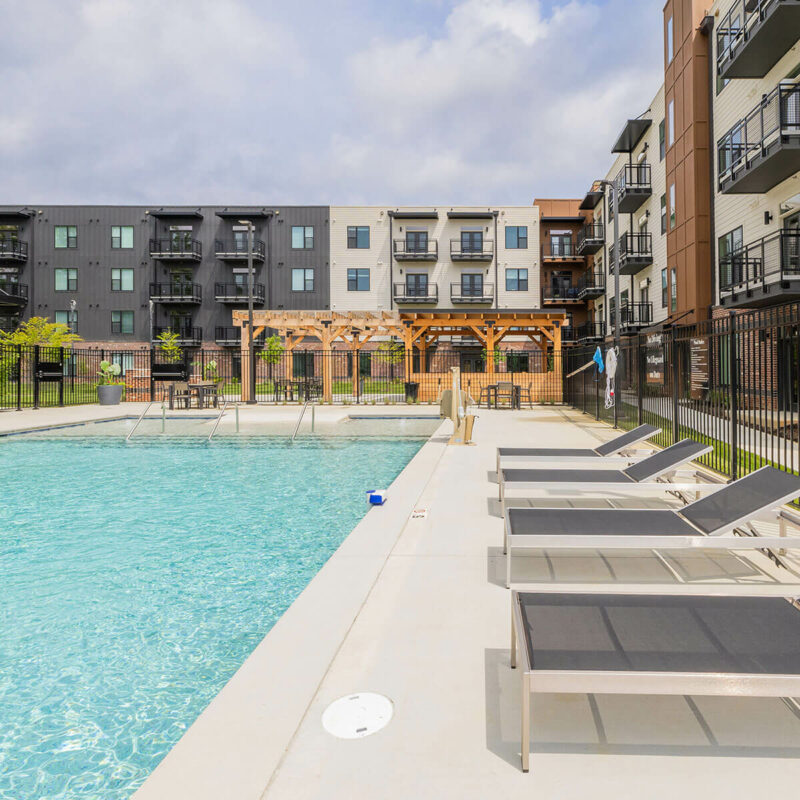 Spacious pool area with loungers, surrounded by modern apartment buildings.