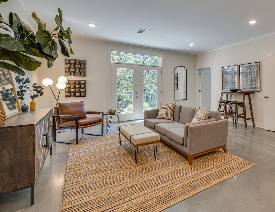 Cozy living room with a sectional sofa, leather chair, and a large rug leading to a sunny patio.